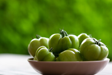Green tomatoes mimicking green apples in a pink bowl with green background