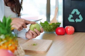 Sustainability. Woman slicing apple in eco-friendly kitchen with recycling bin.