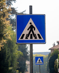 Blue and white sign with a person walking across a crosswalk