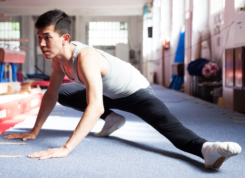 gymnast doing leg stretches - warm up before exercising on sports equipment in gym