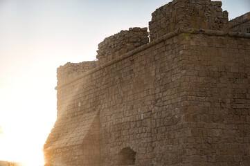 The setting sun is casting a warm glow on the weathered stone walls of a medieval fortress. Paphos, Cyprus