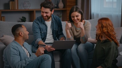 Joyful happy multiracial four friends shopping laptop celebrating achieve applauding yes gesture successful winning money online bet casino at home party on couch diverse men women using credit card
