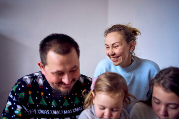 Fototapeta premium a family with daughters toddler and teenager make a Christmas tree from gingerbread cookies and decorate it with white cream and blue sugar snowflakes