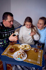 family with daughters toddler and teenager cozy together drinking tea and eating gingerbread Christmas tree