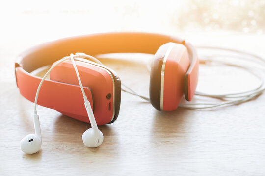 Red headphones and white earphones on a wooden table.[1][2][3] The morning sun shines on the side, creating a warm atmosphere, perfect for music listening and relaxation concepts.