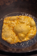 Golden flatbread or dough puffing up as it deep-fries in bubbling hot oil within a dark pan, showcasing rustic and traditional cooking methods. 
