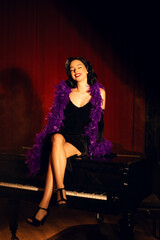 Performing artist in a purple feather boa poses on a grand piano with red curtains in the background during a glamorous evening event
