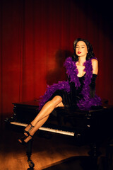 Performing artist in a purple feather boa poses on a grand piano with red curtains in the background during a glamorous evening event