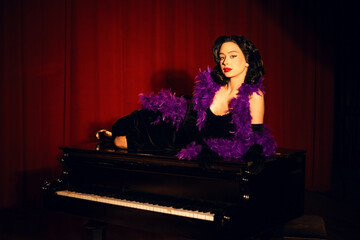 Performing artist in a purple feather boa poses on a grand piano with red curtains in the background during a glamorous evening event