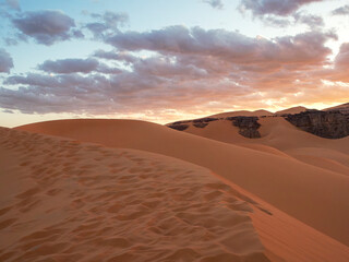 Landscape of the Red Tadrart with dunes and rock formations at sunrise in the Sahara Desert, Algeria.