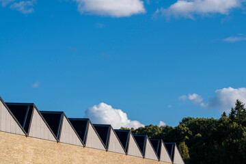 Contemporary roofline architecture with repeating triangular skylights under blue sky and white clouds in Stockholm, showing rhythm and industrial minimal design