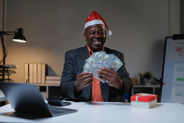 African American businessman in a Santa hat celebrates holiday financial success at his office...