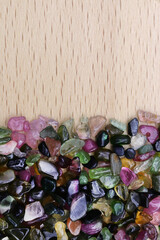 Tourmaline heap jewel stones texture on half light varnished wood background. Place for text.