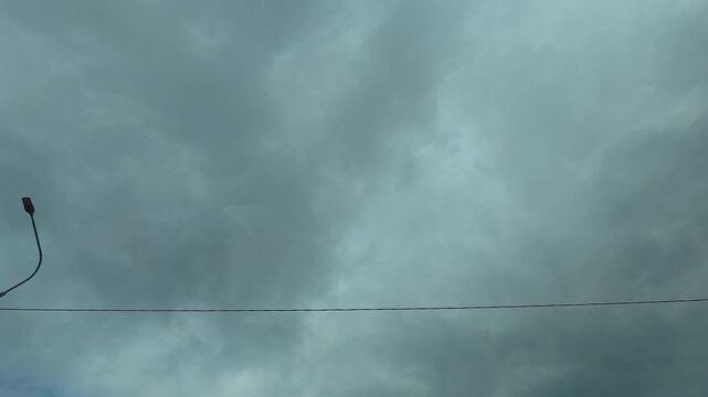View from a moving car of cloudy sky drive near lampposts on road.