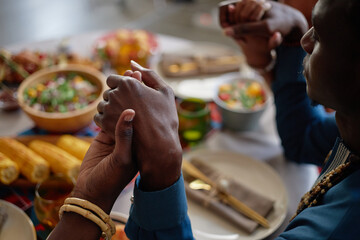 Black man and Black woman holding hands at table during Kwanzaa celebration, engaging in prayer or...