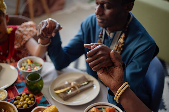 Black man and Black woman holding hands around table during Kwanzaa celebration, joining in unity before meal, visible traditional dishes and festive table setting emphasizing cultural tradition