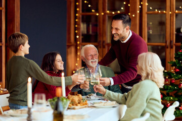 Family And Friends Toast Together At Christmas Dinner By Festive Table With Tree