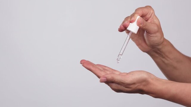 Close-up of female hands dispensing liquid serum or oil from a dropper into the palm for face or hair on a light background. Product application during skincare or haircare routine with copy space.