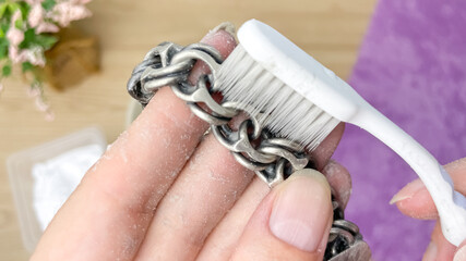 A woman manually polishes a tarnished silver piece with a toothbrush. Cleaning silver at home.