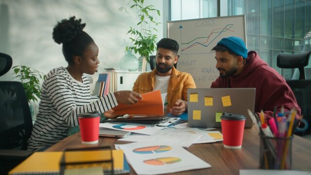 Three business workers team briefing meeting office discuss documents result stats with laptop solving financial budget company problem. Smiling African American informal businesswoman with Hindu men