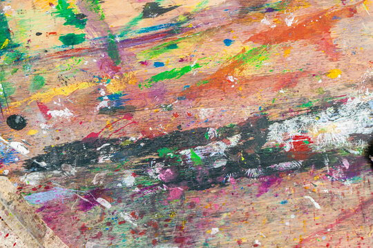 Close-up of messy wooden surface covered in colorful dried paint splashes and brush strokes, flat lay for design. Concept of painting palette, artistic chaos, creative process in visual art workspace