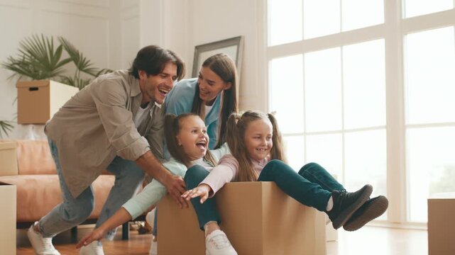 A cheerful family gathers in their new apartment as they unpack moving boxes. The children play with the cardboard boxes while parents assist in arranging their new home.