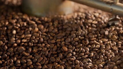 Close up roasted coffee beans mixing in mixer roaster blend automatic metal drum machine stirring roasting cocoa caffeine at production facility aromatic grains in grinder industrial food preparation