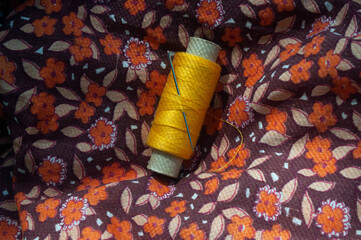A spool of yellow thread and a needle on a floral print cotton fabric backround.