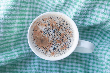 Top view coffee mug with coffee foam and cinnamon on white and green checkered fabric background