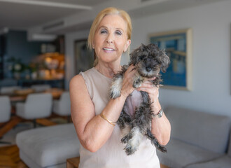 Portrait of a smiling happy senior woman with her little puppy dog looking at camera at home.