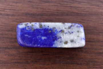 Lapis lazuli jewel stone texture on brown varnished wood background. Macro closeup.