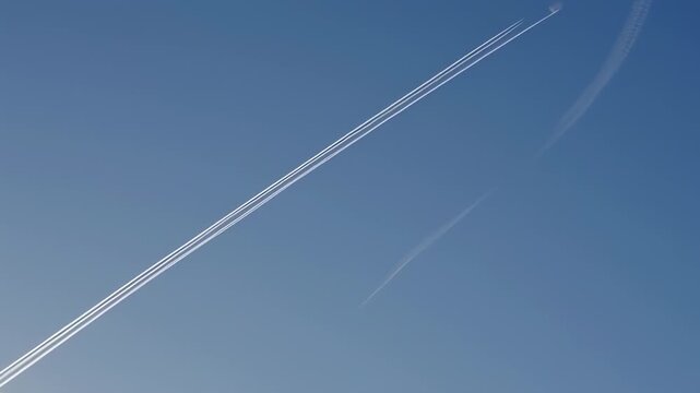 Clear, blue sky with airplane contrails, one thick and one thin, parallel and angled