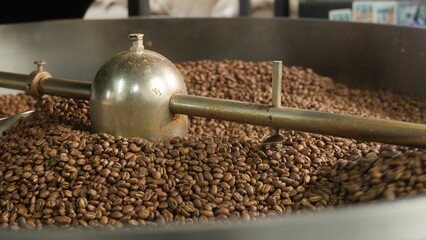 Close up roasted coffee beans mixing in mixer roaster blend automatic metal drum machine stirring...