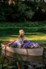 Girl in wooden boat with purple hydrangea flowers on green pond