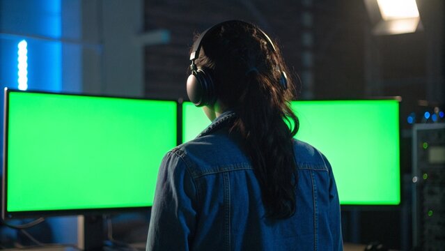 Back View of Female VFX Artist Working on Computer with Dual Green Screen Monitors in Studio
