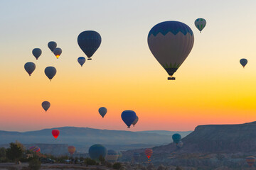 Hot air balloons float over the valleys of Cappadocia at sunrise, creating a colorful view above the rocky landscape.