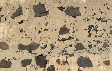 Close-up of aged stucco wall showing rough volcanic stones and cracked surface details