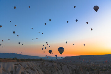 Hot air balloons float over the valleys of Cappadocia at sunrise, creating a colorful view above the rocky landscape.