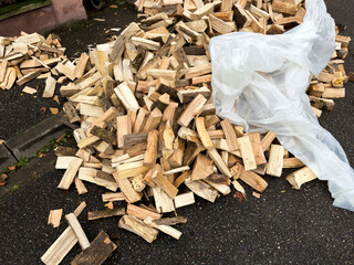 Freshly chopped firewood logs piled on an asphalt driveway with a large plastic sheet partially covering them ready for storage or use as heating fuel