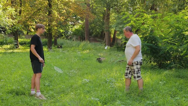 Tilt up shot of father teaching son how to hold badminton racket and explaining rules of game in park on summer day.
