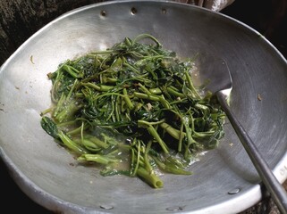 Stir-fried water spinach in a wok with garlic and chili.