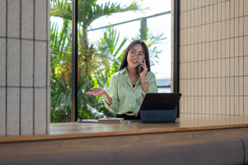 Fototapeta premium Young asian businesswoman talking on phone and gesturing in modern office