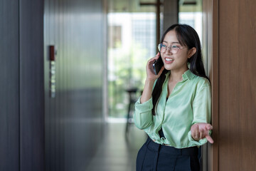 Businesswoman talking on phone near elevator in office hallway
