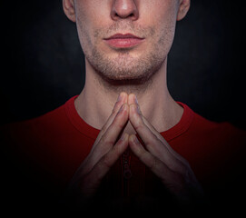 Close-up portrait of a serious man in a red shirt with his fingers forming a triangle gesture, symbolizing confidence and contemplation against a dark background.