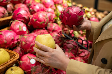 Person selecting fresh pears and dragon fruits in a supermarket