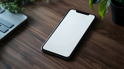 Smartphone with blank screen rests on modern wooden desk, surrounded by laptop and green plants, creating minimalist and serene workspace