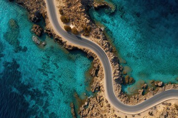 Aerial view of winding coastal road along turquoise blue waters and rocky shoreline