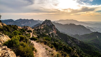 A scenic view of a rugged mountain range under a cloudy sky. A narrow path winds along the ridge, offering a glimpse of the distant coast