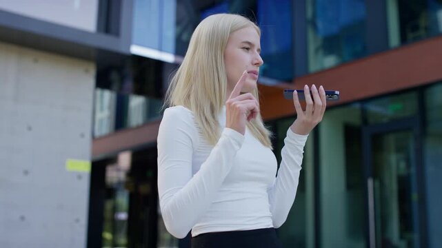Young woman recording voice message on smartphone outside