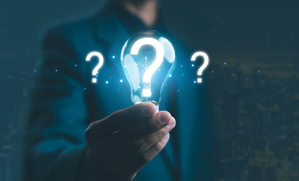 Businessman holding glowing light bulb with question mark symbol, representing innovation, creative thinking, business idea, and problem-solving concept in technology and decision-making strategy.
